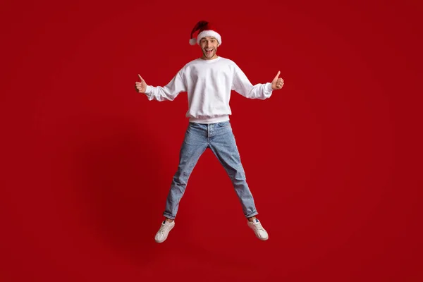 Oferta de Natal. Cara excitado em Santa Hat pulando e gesticulando polegares para cima — Fotografia de Stock
