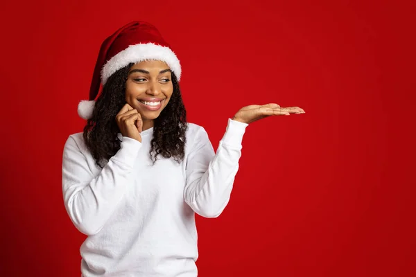 Heureuse dame afro-américaine au chapeau de Père Noël montrant quelque chose de gentil — Photo
