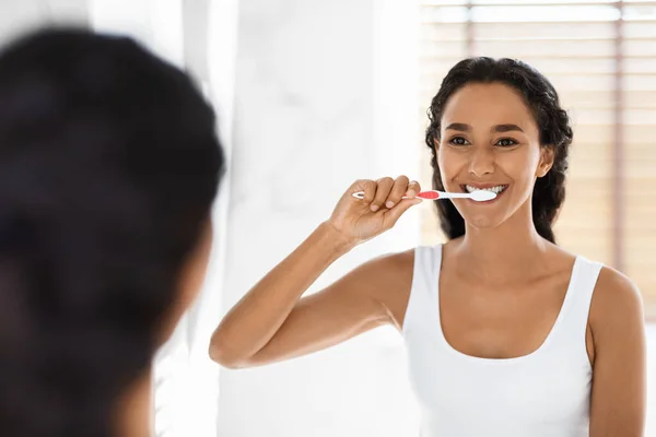 Feliz joven mujer de Oriente Medio cepillándose los dientes con cepillo de dientes en el baño — Foto de Stock