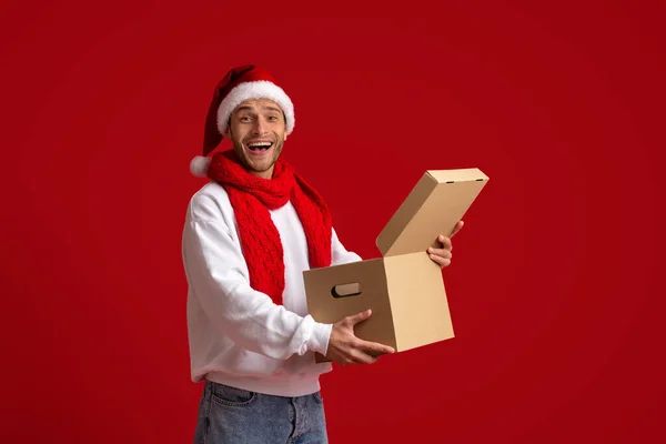 Weihnachtszustellung. Überraschte junge Kerl in Santa Hat Öffnen Paketkasten — Stockfoto