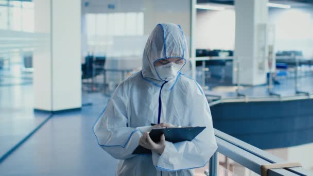 Doctor Wearing Hazmat Suit And Mask Taking Notes In Clinic — Stock Video