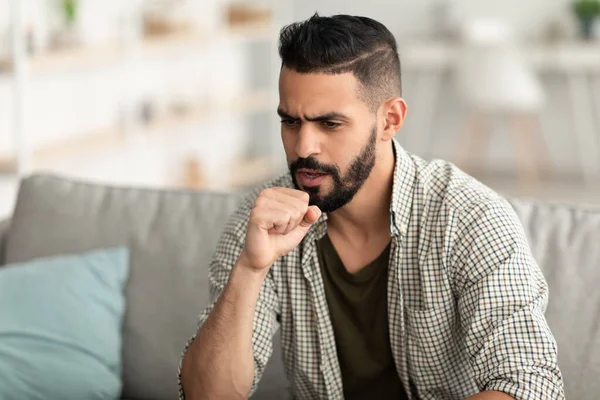 Coronavirus, mevsimsel grip. Hasta Arap yumruk yumruğa öksürüyor, kanepede oturuyor, kendini iyi hissetmiyor, boş yer var.