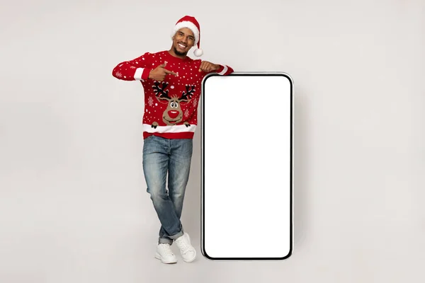 Lächelnder afrikanisch-amerikanischer Mann mit Weihnachtsmütze und Smartphone-Attrappe — Stockfoto