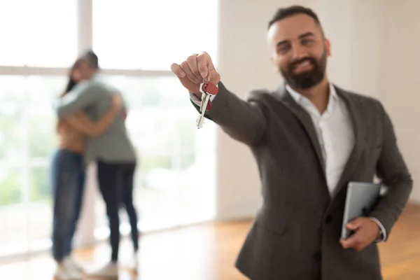 Sonriente agente de bienes raíces sosteniendo y mostrando clave — Foto de Stock