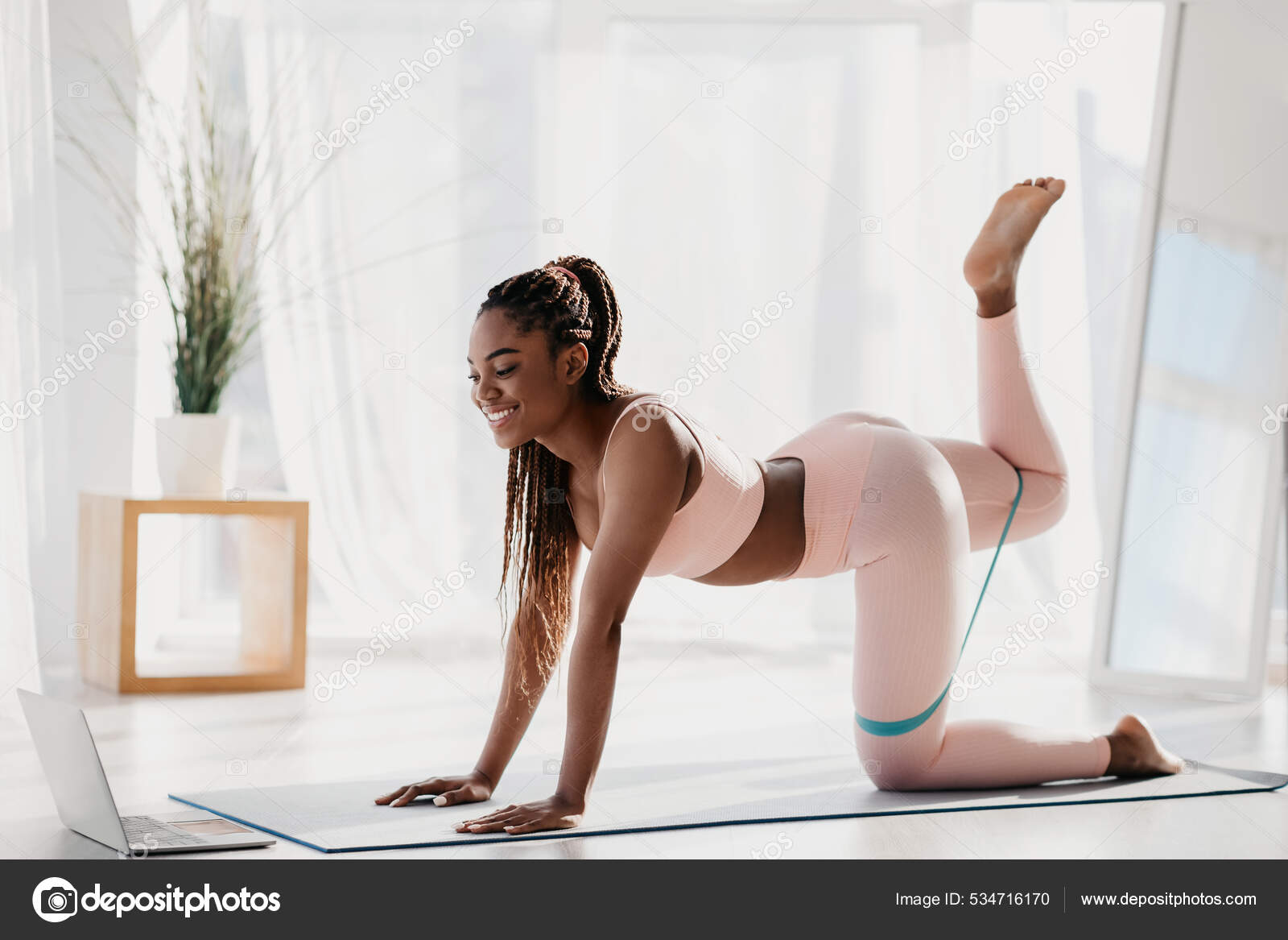 Young black woman working out her butt muscles in front of laptop, using elastic band, following video tutorial at home Stock Photo by ©Milkos 534716170