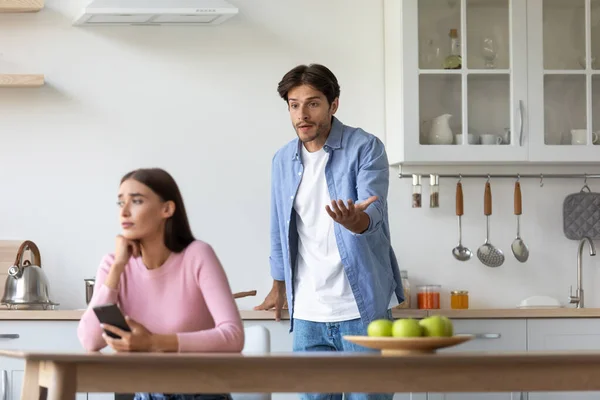 Triste millennial europea mujer con teléfono inteligente ignora ofendido enojado gritando marido en la cocina — Foto de Stock