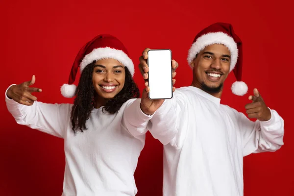 Beautiful black couple in Santa hats showing smartphone, mockup — Stock Photo, Image