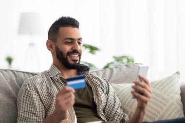 Siber alışveriş konsepti. Cep telefonu ve kredi kartıyla evden mal sipariş eden bin yıllık Arap bir adam.