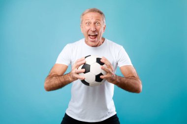 Olgun adam mavi arka planda futbol topuyla poz veriyor