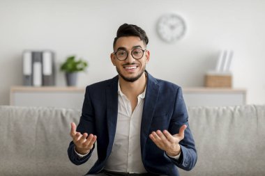 Orta Doğulu genç bir psikoloğun portresi kameraya gülümsüyor, ofisteki rahat koltukta oturuyor.