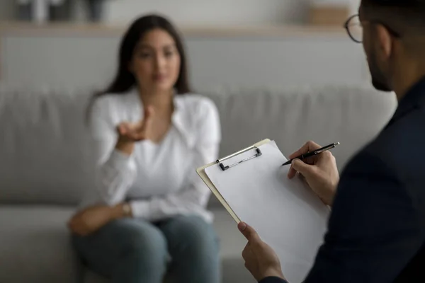 Mujer árabe estresada consultando psicóloga en consultorio médico, psiquiatra tomando notas durante la sesión —  Fotos de Stock