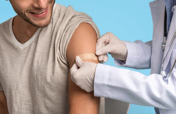 Лікар накладає пластир на плече молодого чоловіка після ін'єкції вакцини — стокове фото