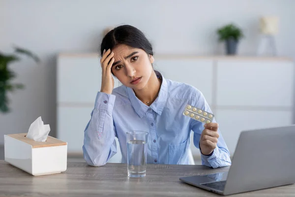 Unhappy upset young indian woman sick, suffering from headache, colds and flu holds pills in office interior — Stock Photo, Image