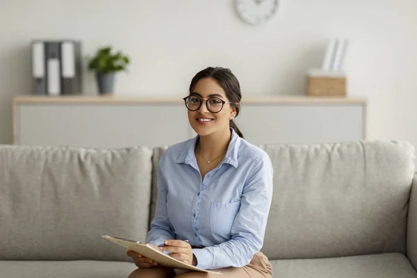 Vrolijke arabische vrouwelijke psycholoog schrijven in klembord, een sessie met de klant, notities maken tijdens overleg — Stockfoto