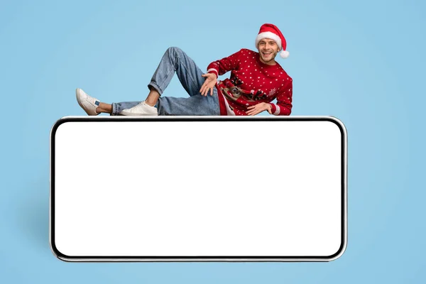 移动广告。快乐的家伙穿着圣诞老人帽躺在大大的空白智能手机之上 — 图库照片