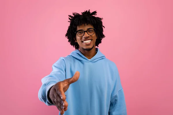 Adolescente preto sorridente oferecendo cumprimentos de aperto de mão no fundo do estúdio rosa. Conceito de parceria, negócio ou acordo — Fotografia de Stock