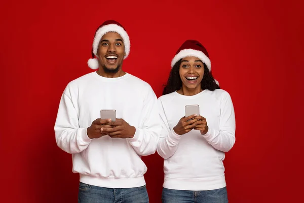 Beau couple noir dans Santa chapeaux en utilisant des smartphones — Photo