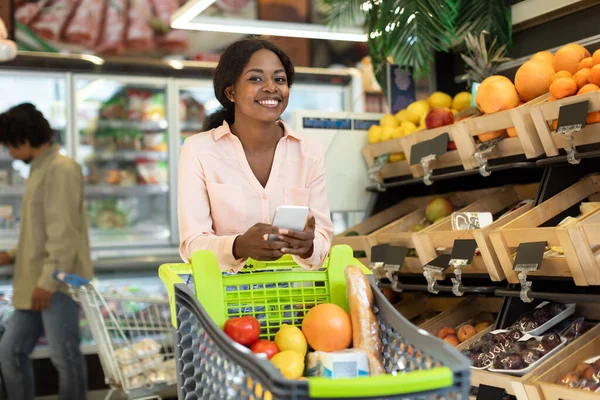 アフリカの女性が携帯電話を持ってスーパーマーケットで食料品の買い物をする — ストック写真