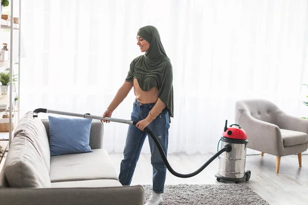 Весела мусульманка чистить диван з пилососом — стокове фото