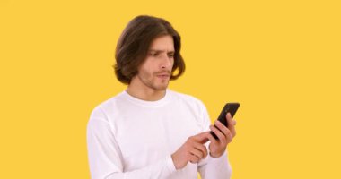 Genç ciddi bir adam cep telefonuyla iletişim kuruyor, internette kötü haberler okuyor ve inançsızlıkla kafasını sallıyor, turuncu arka plan