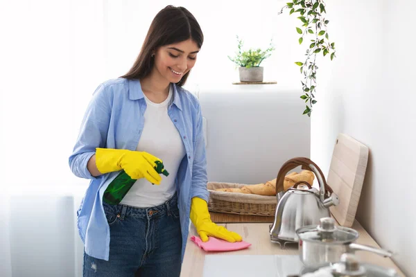 Joyeux jeune femme nettoyage table de cuisine avec chiffon — Photo