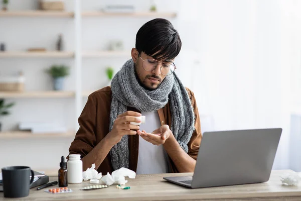 Sick guy taking medicine while sitting in front of laptop — Stock Photo, Image