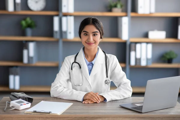 Vidám millenniumi indiai női orvos fehér köpenyben munka a munkahelyen a klinikán iroda belső laptoppal — Stock Fotó