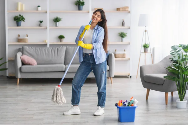 Porträt einer aufgeregten Frau, die singend den Boden putzt und einen Wischmopp hält — Stockfoto