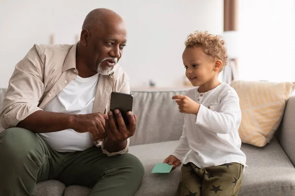 Afro-americano vovô mostrando smartphone para neto em casa — Fotografia de Stock