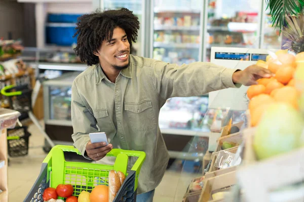 スーパーマーケットでスマートフォンショッピング食料品を使用して幸せなアフリカの男 — ストック写真