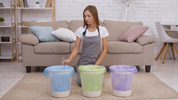 Jovem dona de casa positiva colocando garrafa de vidro em caixote do lixo azul em casa, apoiando a conservação do ambiente — Vídeo de Stock