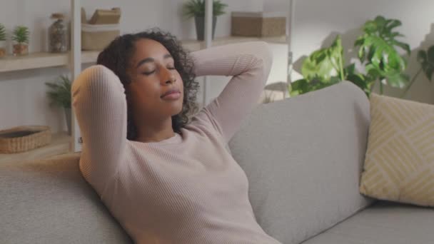 Meditation og afslapning koncept. Ung afrikansk amerikansk kvinde hviler sig hjemme, afslappende på sofaen med lukkede øjne – Stock-video