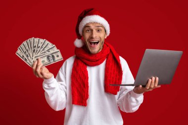 Yeni Yıl Piyangosu. Noel Baba Şapkalı Adam 'ın elinde para ve dizüstü bilgisayar var.