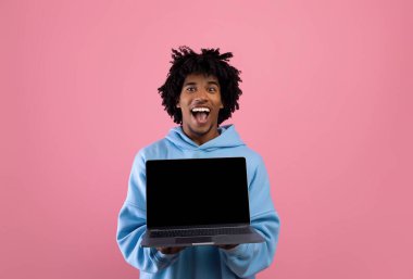 Pembe stüdyo arka planında boş siyah ekranlı dizüstü bilgisayarı olan heyecanlı genç adam, web sitesi için maket.