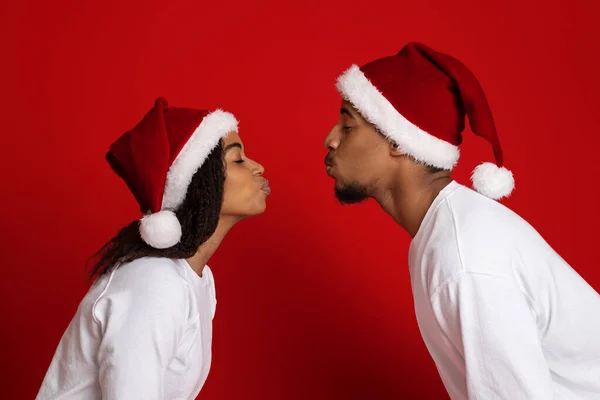 Negro hombre y mujer en Santa sombreros besos en rojo — Foto de Stock