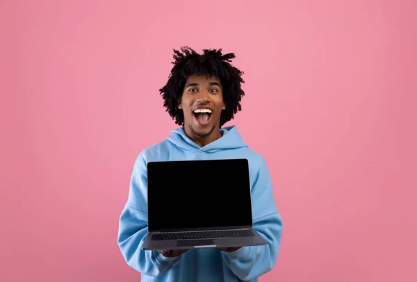 핑크 스튜디오 배경에 빈 블랙 스크린 이 있는 노트북을 들고 있는 흥분된 흑인 10 대 남자 웹 사이트 momoup — 스톡 사진