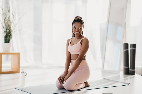 Lächelnde junge schwarze Frau, die zu Hause trainiert, Pause macht, sich drinnen auf einer Yogamatte ausruht, volle Länge — Stockfoto