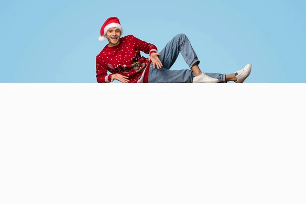 Vakantie advertentie. Vreugdevolle man in Santa Hat liggend boven blanco Advertentie Board — Stockfoto