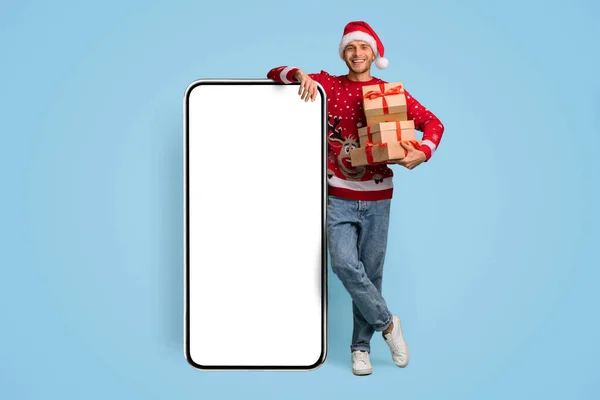 Gelukkig man met kerstcadeaus in handen staan in de buurt van Big Blank Smartphone — Stockfoto