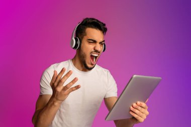 Duygusal genç Arap adam spor takımının yenilgisinden hayal kırıklığına uğradı, neon ışıklı tablet bilgisayarında maç seyrediyor.