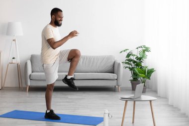 Mutlu genç Afro-Amerikan sakallı erkek paspas üzerinde bacak egzersizi yapıyor.