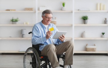 Tekerlekli sandalyedeki son sınıf öğrencisi evde tablet bilgisayar ve kredi kartıyla online alışveriş yapıyor.