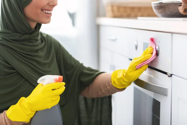 Крупним планом усміхнена молода мусульманка прибирає піч на кухні — стокове фото