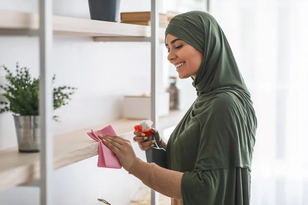 Musulmana giovane donna pulizia scaffali con detergente a casa — Foto Stock