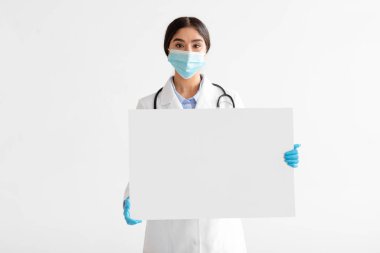 Paltolu ve koruyucu maskeli genç Hintli kadın doktor boş alanlı büyük kağıt pankart tutuyor.