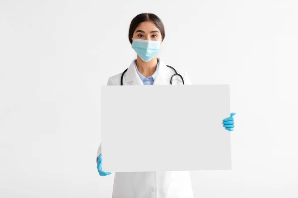 Joven médico indio con abrigo y máscara protectora sostienen pancarta de papel grande con espacio vacío —  Fotos de Stock