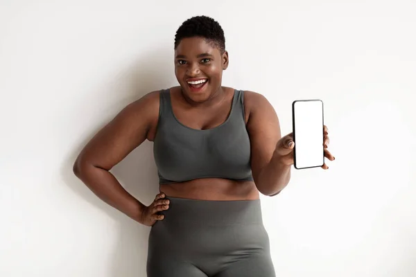 Sorrindo esportivo afro-americano plus size mulher mostrando celular, mockup — Fotografia de Stock