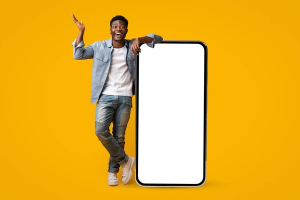 Emotionaler afrikanisch-amerikanischer Mann steht neben großem Smartphone, Attrappe — Stockfoto