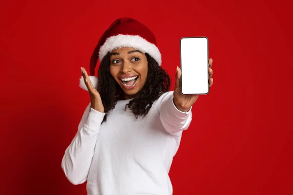 Thrilled black lady in Santa hat showing cellphone, mockup — Stock Photo, Image