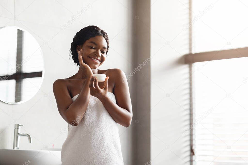 Sensual black lady applying cream on her face after shower